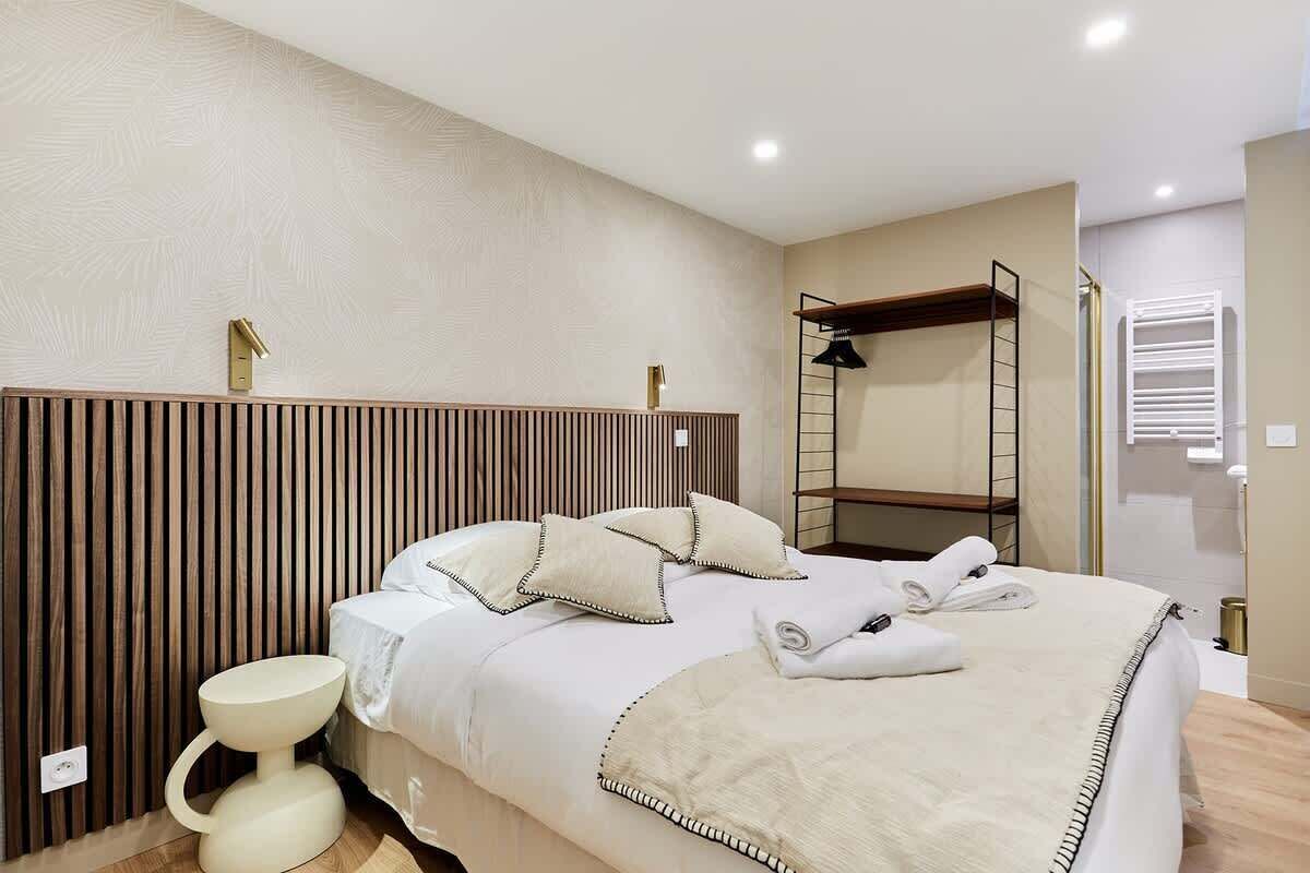A hotel room with a bed, a bedside table, a towel rack, and a shower area.