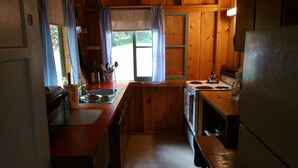 Une cuisine de taille réduite avec des murs en bois, un évier, une cuisinière et un réfrigérateur.