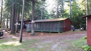 Une cabane à l’extérieur vert, dotée d’une grande façade vitrée et entourée de grands arbres.