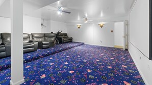 Een bioscoopzaal met een blauw tapijt, leren fauteuils, plafondventilatoren en wandluidsprekers.