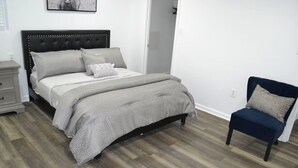 Een slaapkamer met een bed, nachtkastje, stoel en een aan de muur hangend schilderij.