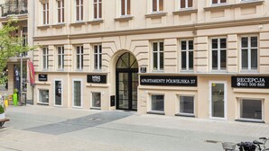 Un immeuble à plusieurs étages, de style architectural classique, avec une entrée centrale dotée d’une porte noire, de nombreuses fenêtres et une enseigne indiquant qu’il s’agit d’un immeuble d’appartements.