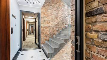 A modern interior with a staircase against a brick wall, a hallway with a geometric floor pattern, and a ceiling with a unique light fixture.