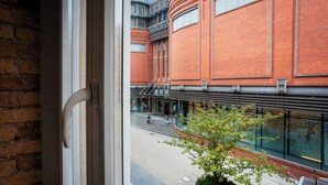 Une vue depuis une fenêtre donnant sur une cour intérieure, avec un bâtiment en briques, un escalier et un petit arbre.
