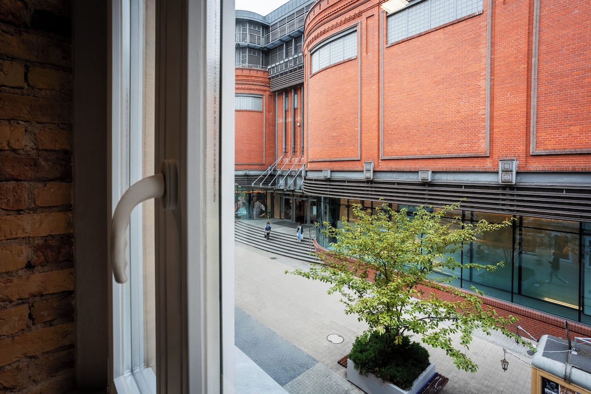 A view from a window overlooking a courtyard with a brick building, a staircase, and a small tree.