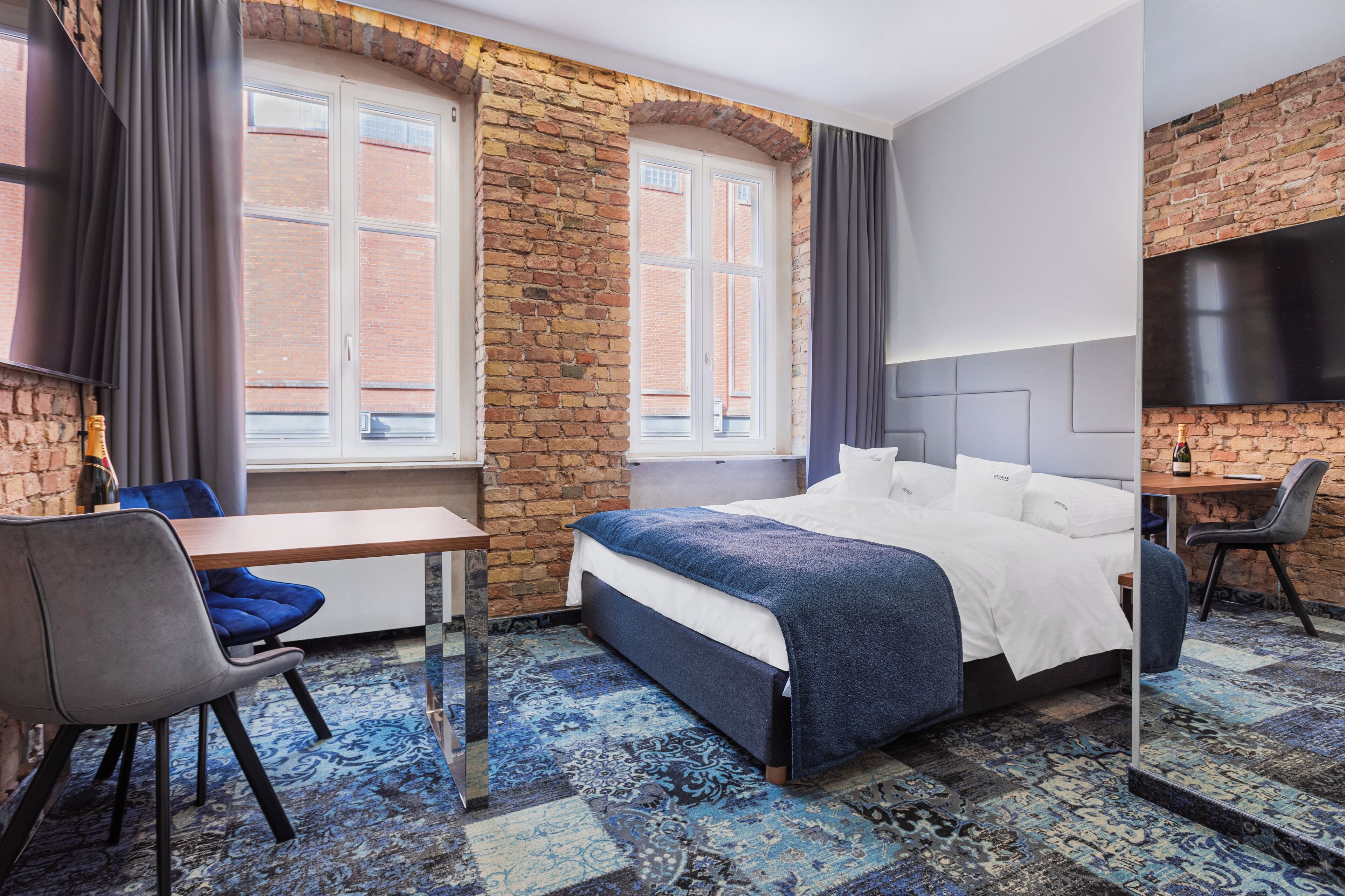 Una habitación de hotel con pared de ladrillo, una cama grande, un escritorio y un televisor montado en la pared.