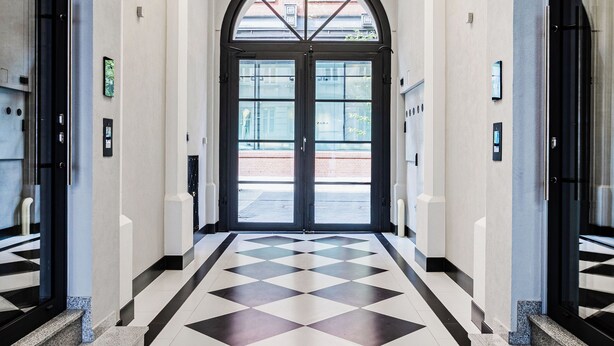 Un couloir doté d’un sol à carreaux, d’une grande porte en arc de cercle et d’un lustre.