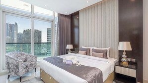 Et moderne hotelværelse med en stor seng, to sengeborde med lamper, en stol og udsigt til bybilledet gennem store vinduer.