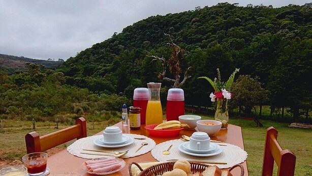 A wooden deck with a table set for breakfast, including plates, bowls, and a basket of bread. - Refuge in the mountains/near the trail to Pico do Papagaio Garcias Peak and Waterfall (Aiuruoca)