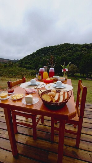 A wooden deck with a table set for breakfast, including plates, bowls, and a basket of bread. - Refuge in the mountains/near the trail to Pico do Papagaio Garcias Peak and Waterfall (Aiuruoca)
