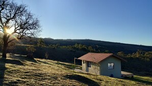 A small house with a red roof on a grassy hill, surrounded by trees and hills in the background. - Refuge in the mountains/near the trail to Pico do Papagaio Garcias Peak and Waterfall (Aiuruoca)