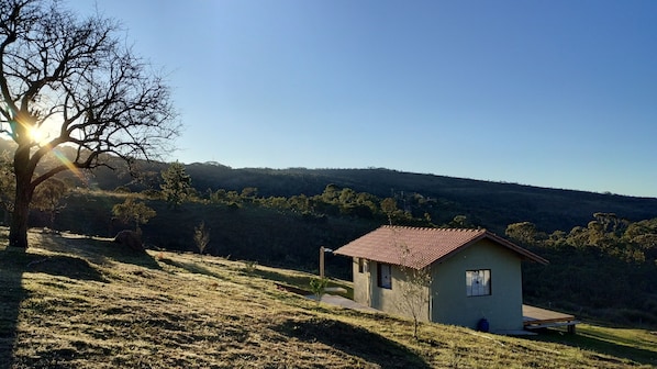 A small house with a red roof on a grassy hill, surrounded by trees and hills in the background. - Refuge in the mountains/near the trail to Pico do Papagaio Garcias Peak and Waterfall (Aiuruoca)