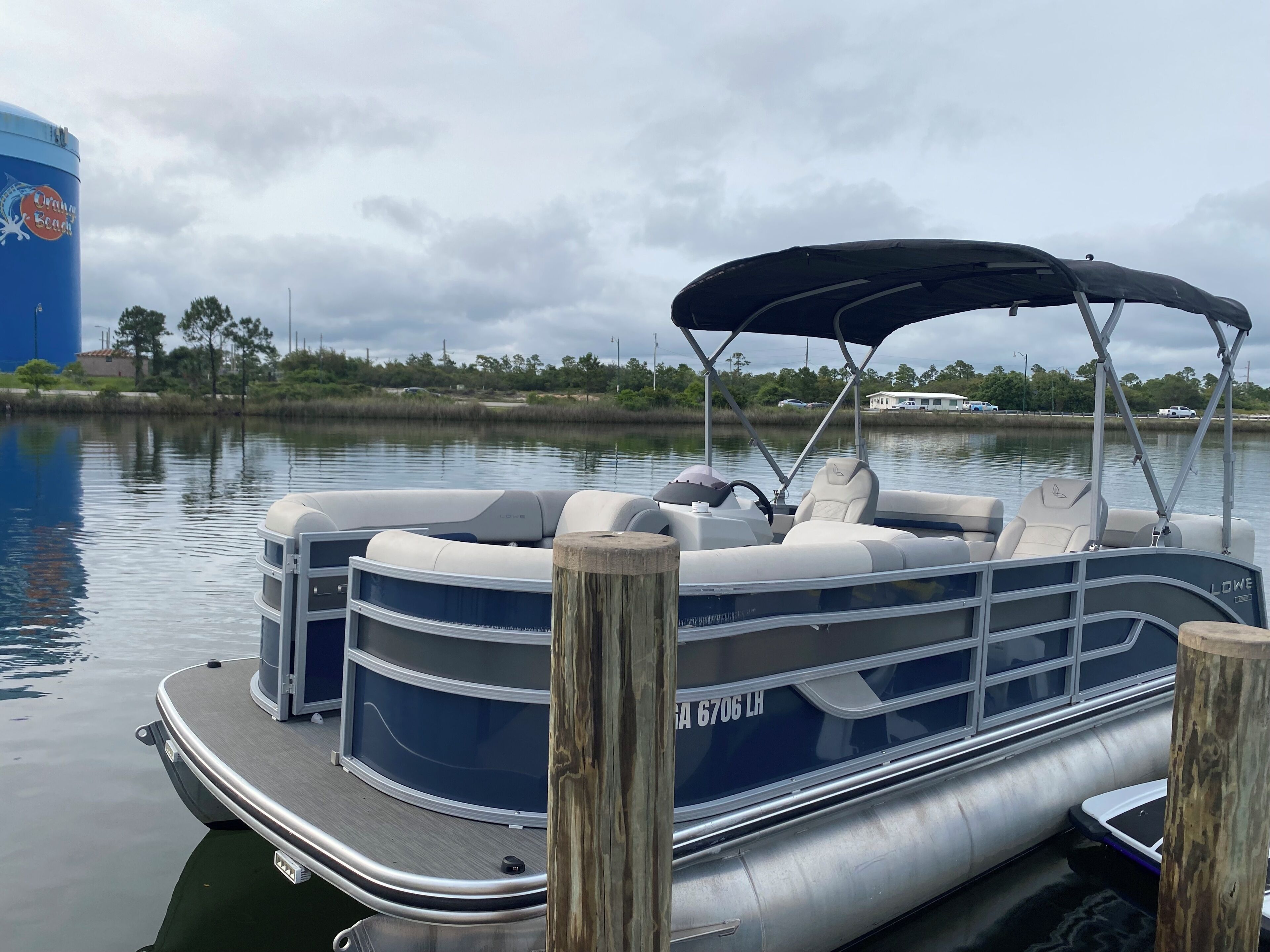 Un barco pontón atracado en un muelle, con un toldo, una cabina con asientos y un depósito de agua al fondo.