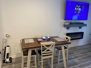 A dining area with a wooden table, chairs, a TV mounted on the wall, a fire feature below, and a mobility scooter.