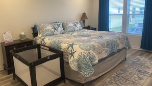 Ein Schlafzimmer mit einem Bett, einem Nachttisch, einer Lampe, einem Deckenventilator und einem Fenster mit Vorhängen.