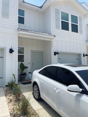 A white two-story house with a garage, a driveway, and a white car parked in front.