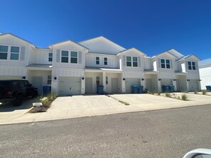 A row of white townhouses with garage doors, a driveway, and a parked SUV. - 3 BR OBA Brand New. Only 1 mile from wharf amphitheater on Canal Great location. (Orange Beach)
