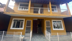 Un edificio de dos pisos con balcón, antena parabólica y entrada con reja.