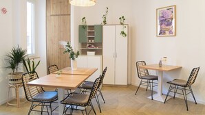 Ruokailutila, jossa on puinen pöytä ja tuolit, riippuvalaisin sekä kasveilla koristeltu kaappi.