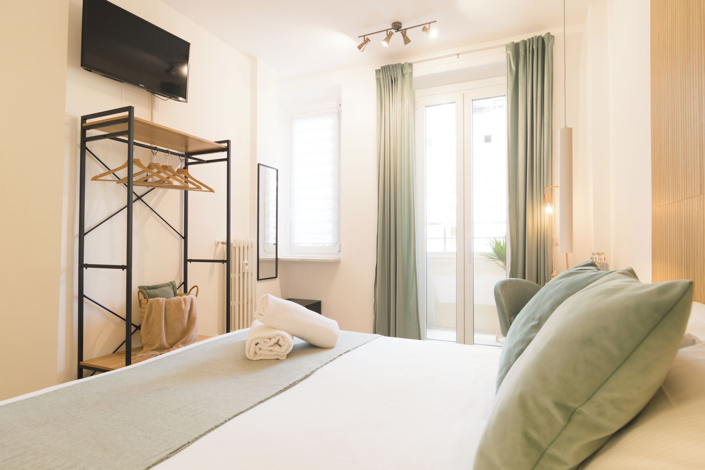 Habitación de hotel con cama, televisor montado en la pared, ventana con cortinas y vistas al exterior.