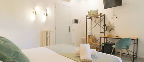 A hotel room with a bed, a desk, a chair, a TV, and a radiator.