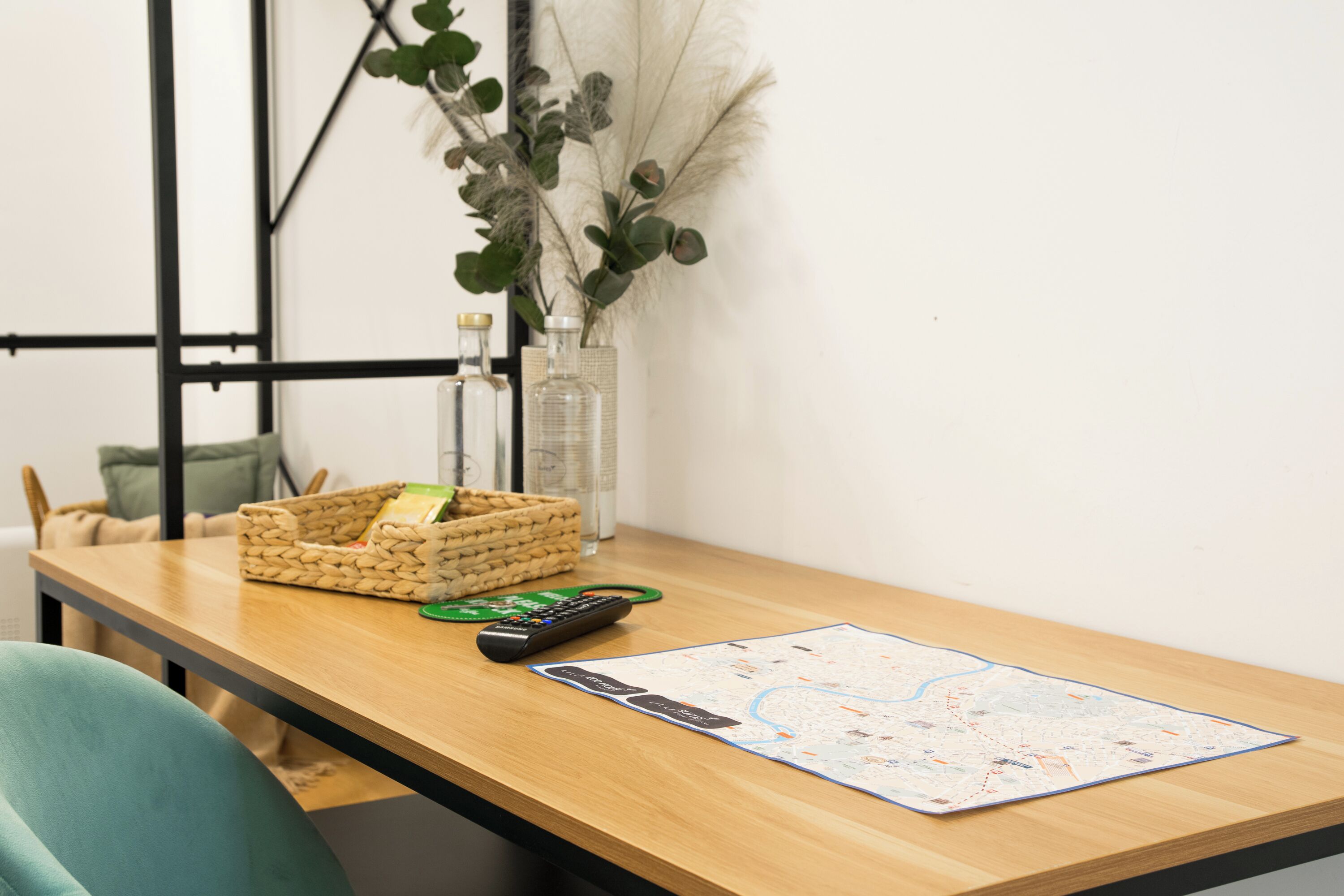 A wooden table with a map, a remote control, a basket, and a vase with plants.