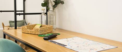 A wooden table with a map, a remote control, a basket, and a vase with plants.