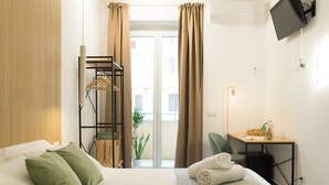 Hotellihuone, jossa on sänky, työpöytä, tuoli, televisio ja parveke, jossa on verhot.