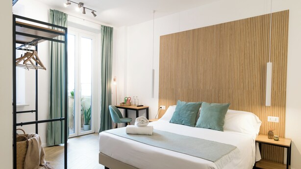 Moderni hotellihuone, jossa on suuri sänky, puinen pääty, työpöytä tuolilla ja lasiovesta avautuva näkymä ulos.