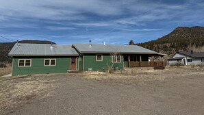 A two-story green house with a metal roof, a wooden porch, and a small front yard. - Wharton Wilderness Ranch House (South Fork)