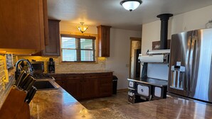 A kitchen with granite countertops, stainless steel appliances, wooden cabinets, a window with blinds, and a built-in stove. - Wharton Wilderness Ranch House (South Fork)