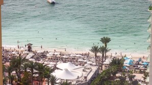 Un complexe hôtelier de bord de mer doté de nombreux parasols, de chaises longues et d’un grand bâtiment blanc surmonté d’une coupole.
