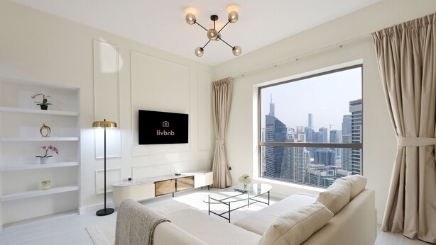 Un salon moderne avec un canapé, un téléviseur fixé au mur, une vue sur la ville à travers de grandes fenêtres et un décor minimaliste.