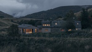 Una casa de piedra rústica con una cabaña de madera, rodeada de campos y colinas cubiertas de hierba.