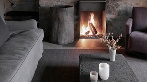 Un salón acogedor con pared de piedra, chimenea, sofá gris, mesa de centro oscura y sillón morado.