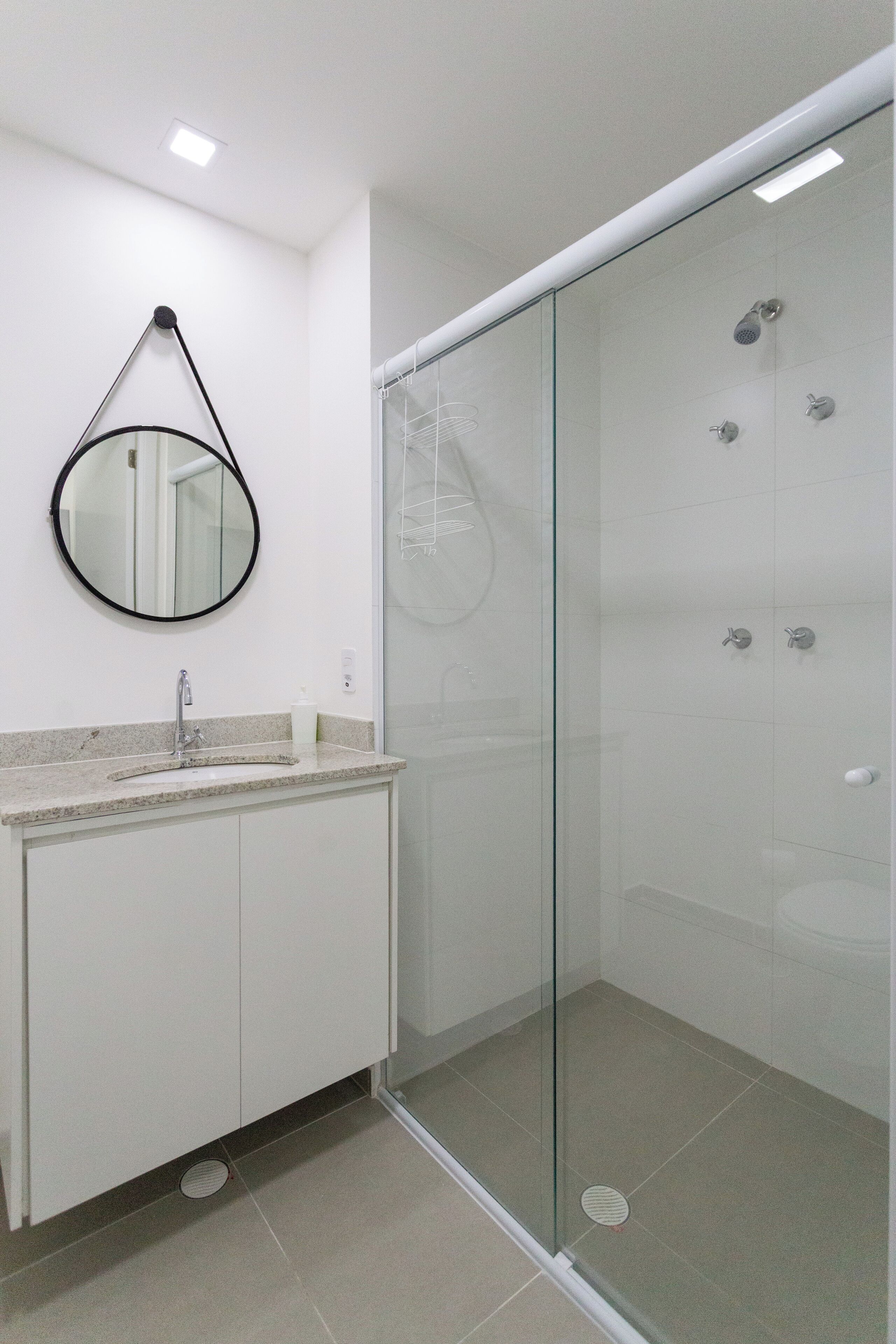 A modern bathroom with a glass-enclosed shower, a round mirror, and a white sink.