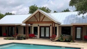 A building with a pool, covered patio, and red chairs.