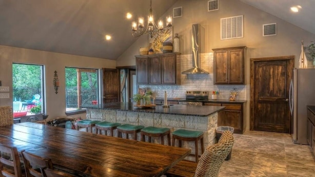A spacious kitchen with a large island, dark wooden cabinets, and a chandelier.