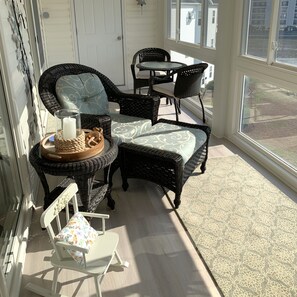 A sunlit room with wicker furniture, a small table with a candle, and a view of the outside.