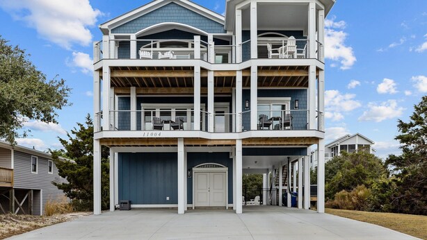 A multi-story house with a covered front porch, a garage, and a balcony with outdoor furniture. - Ocean Views & Surf Fishing Paradise at The Point – Perfect Family Escape! (Emerald Isle)