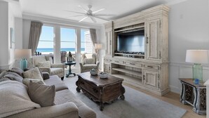 Ein geräumiges Wohnzimmer mit großem Fernseher, bequemen Sitzgelegenheiten und Blick auf den Ozean.