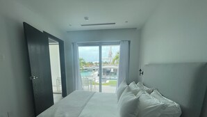A hotel room with a bed, a nightstand, and a view of a pool and outdoor area. - The Seashell Condo (Nassau)