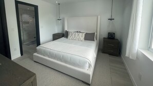 A modern bedroom with a large bed, bedside tables, a walk-in closet, and a large window. - The Seashell Condo (Nassau)