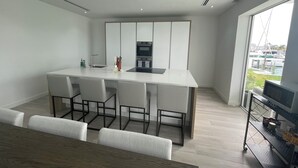 A modern kitchen with a central island, bar stools, and a dining table with chairs. - The Seashell Condo (Nassau)