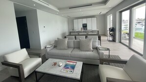 A modern living room with a sofa, armchairs, a coffee table, and a view of a marina through large windows. - The Seashell Condo (Nassau)