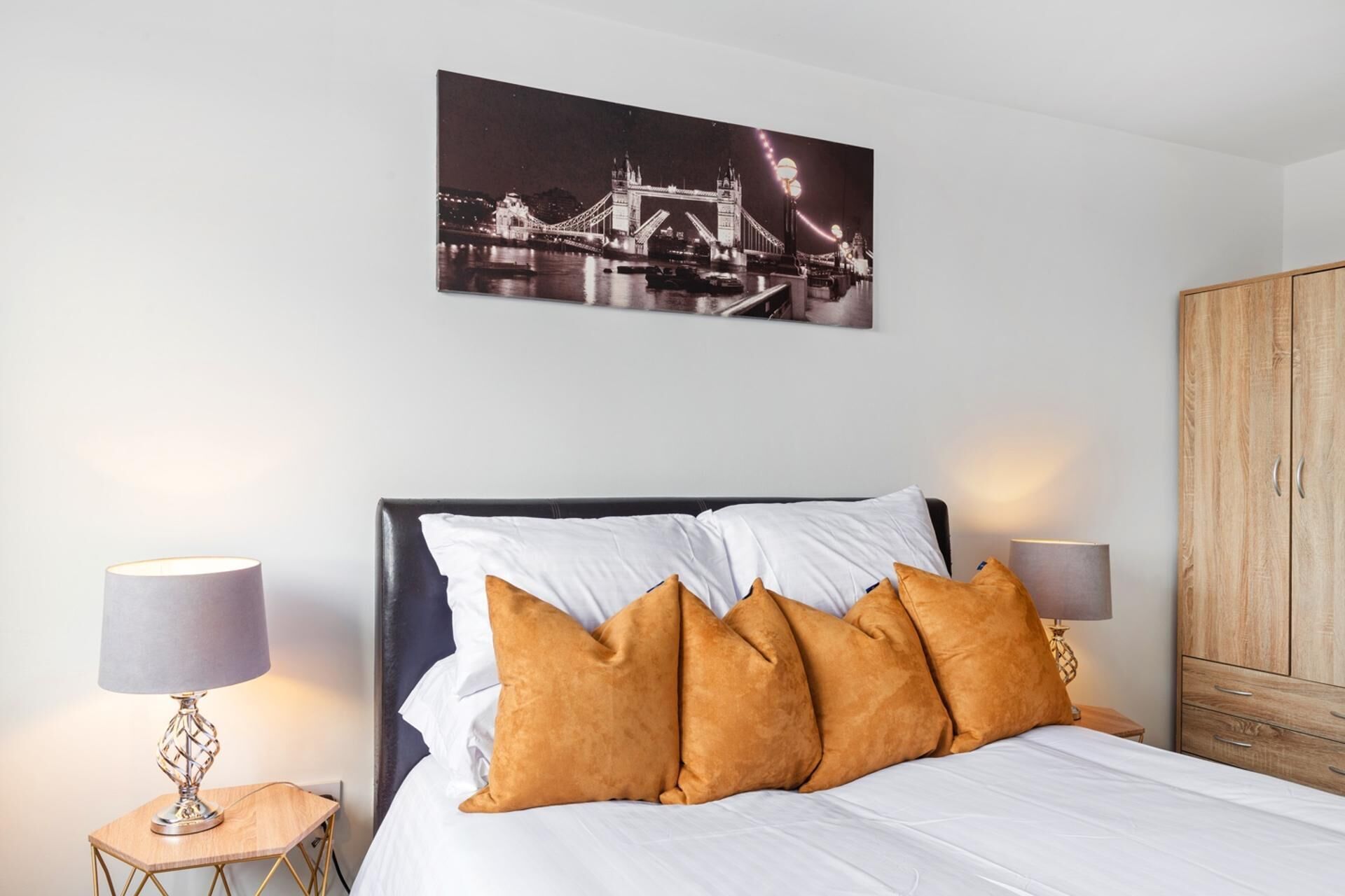 A hotel room with a bed, white bedding, a black headboard, and a large picture of a bridge at night.