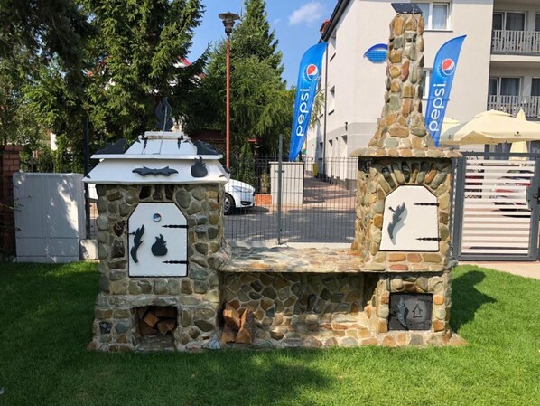 Une cheminée extérieure en pierre, dotée de deux foyers, entourée d’un muret de pierre et d’une zone herbeuse.