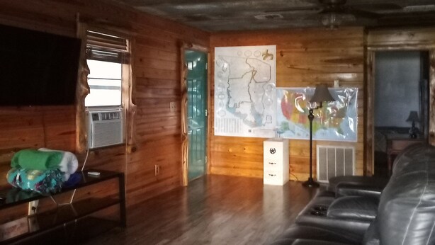 Interior de madeira com ventilador de teto, um mapa na parede, um sofá e uma mesa com abajur.