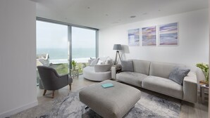 A modern living room with a large window overlooking the ocean, a grey sofa, a round chair, and a lamp. - At 1 Island Reach, you'll find yourself just steps away from pristine beaches (Newquay)
