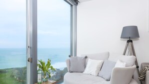 A modern living room with a large window offering a view of the ocean. - At 1 Island Reach, you'll find yourself just steps away from pristine beaches (Newquay)